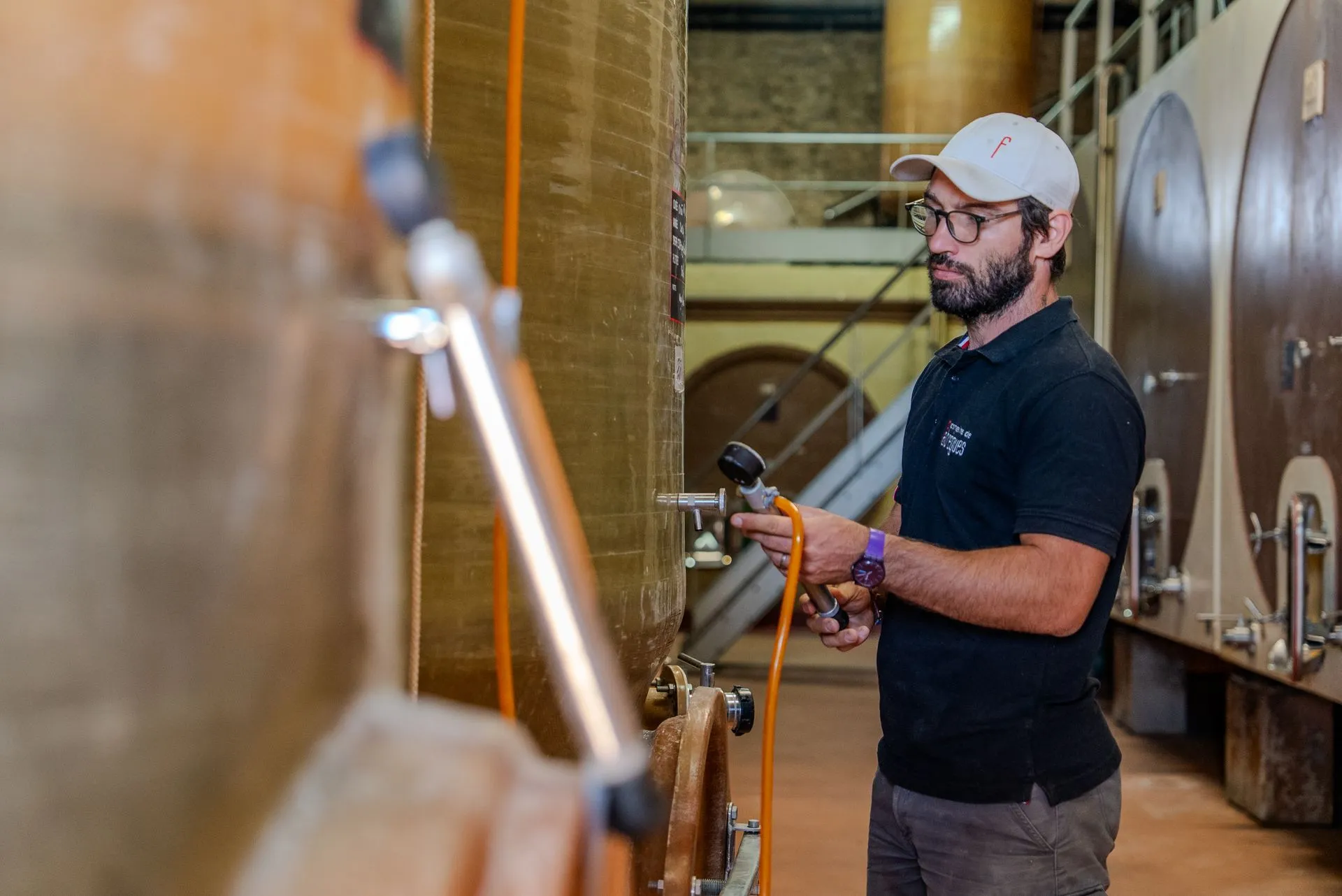 Arthur branche un tuyau sur une cuve de la cuverie